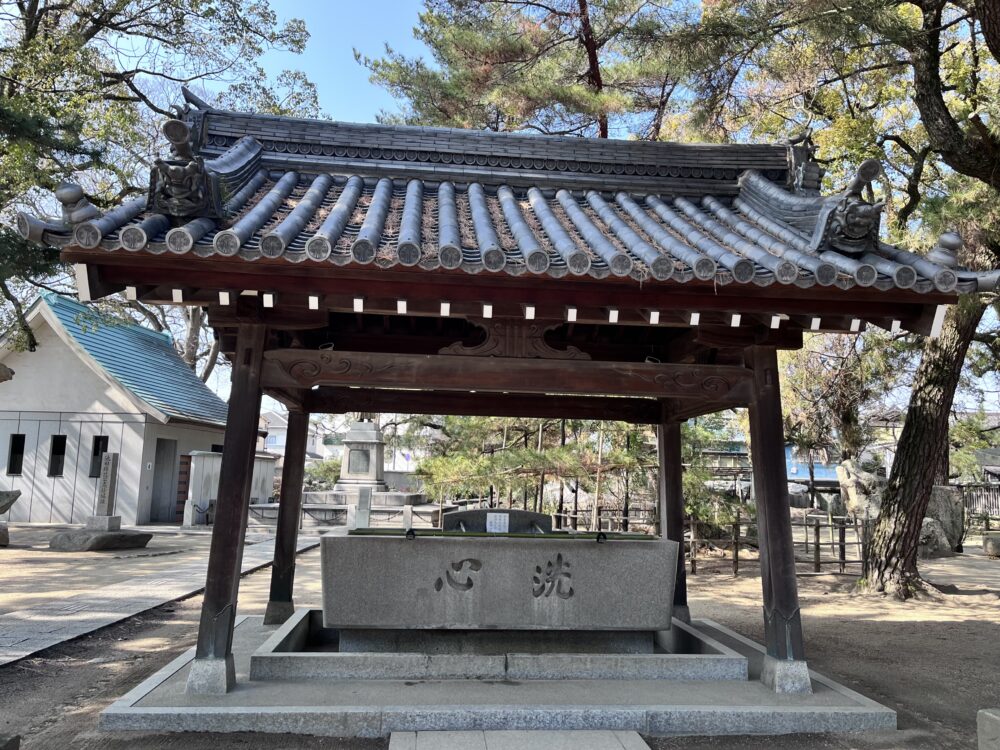 高砂神社の手水舎。屋根付きで松に囲まれた落ち着いた参拝前の清めの場所